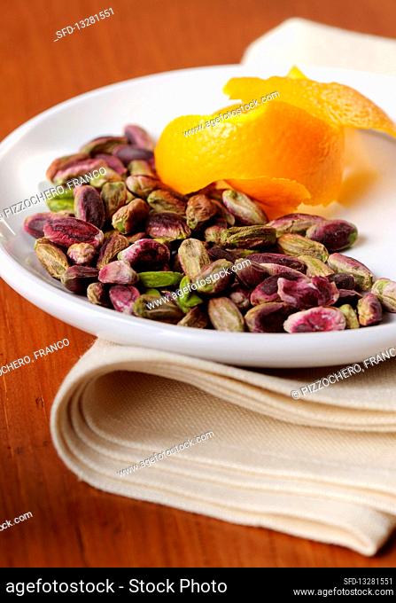 Peeled pistachios on a white plate with orange peel
