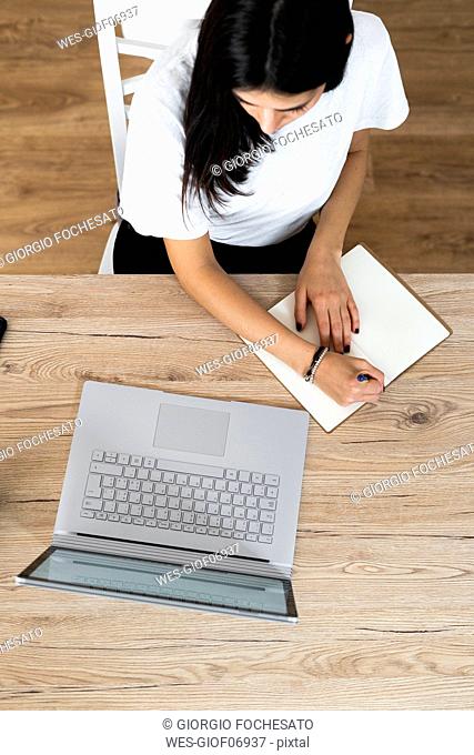 Top view of young woman with laptop taking notes