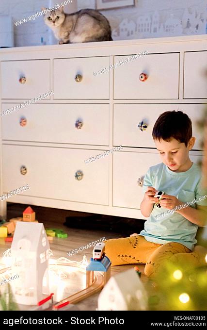 Boy playing with toy train in front of white cabinet at home