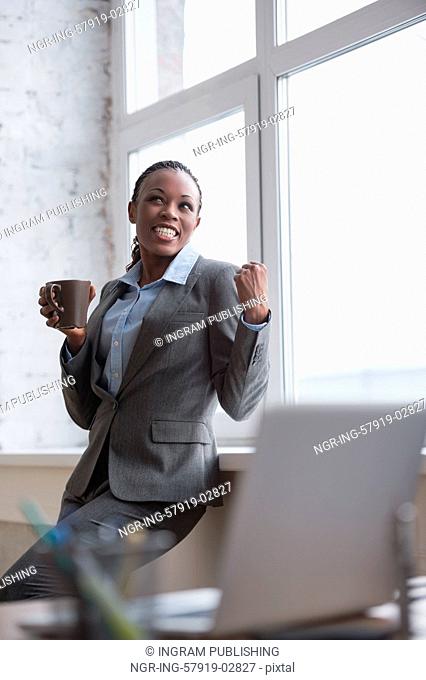 Portrait of smiling african business woman at her office with coffee cup celebrating success and expressing happiness joy and positivity