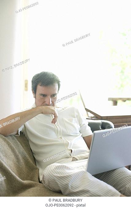 Man sitting on living room sofa with laptop thinking