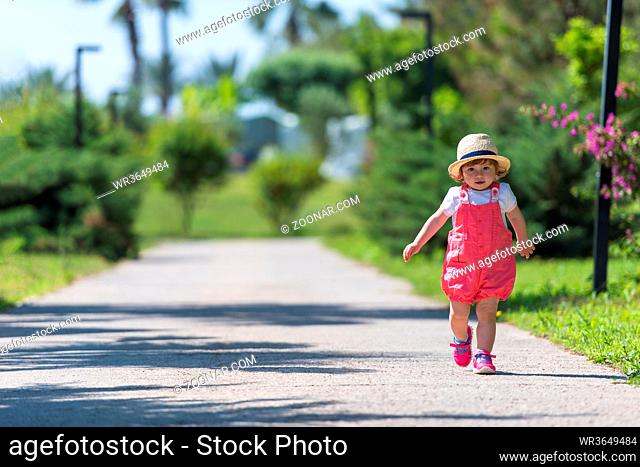 cute little girl with hat cheerfully spending time while running at Park on the summer morning