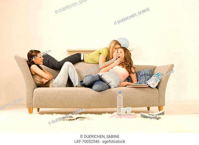 Three teenage girls (14-16) sitting on sofa and talking