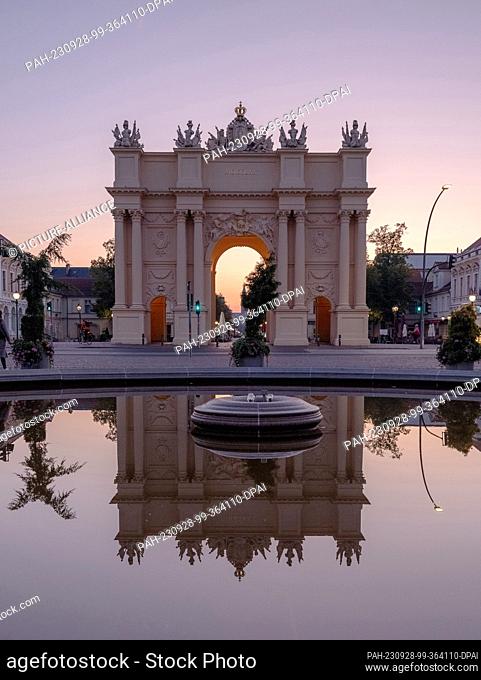 28 September 2023, Brandenburg, Potsdam: Behind the Brandenburg Gate in Potsdam, the sky turns colorful at sunrise. Temperatures of up to 27° C are forecast for...