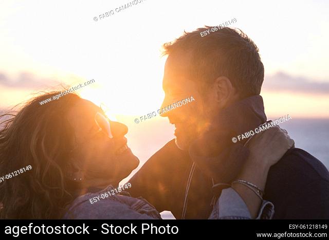 Young romantic couple embracing outdoors during sunset. Close up of loving couple spending leisure time on holiday. Smiling affectionate couple looking at each...