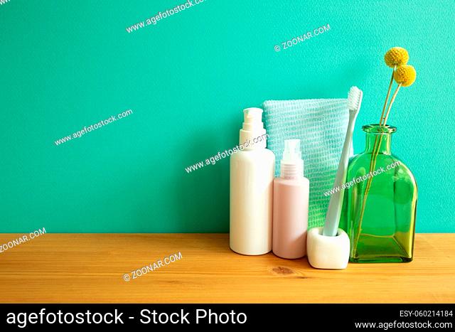 Bathroom bottles, shower towel, toothbrush, vase of plant on wooden table. mint wall background. Skin care and spa concept