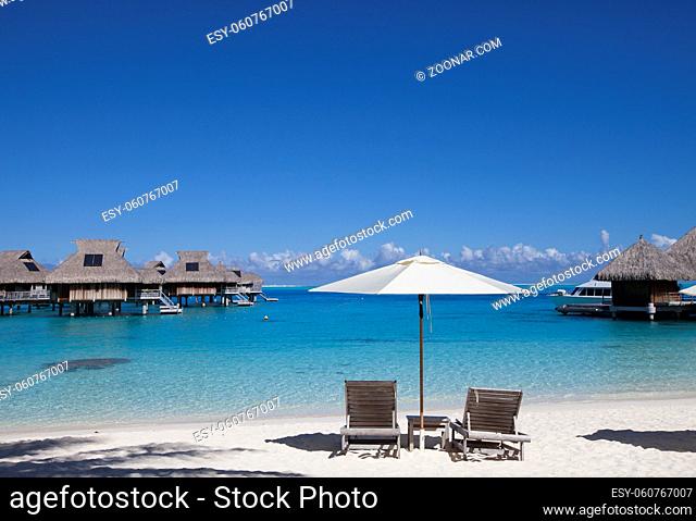 beach chairs and sun umbrella on the beach and houses over the sea. Tahiti