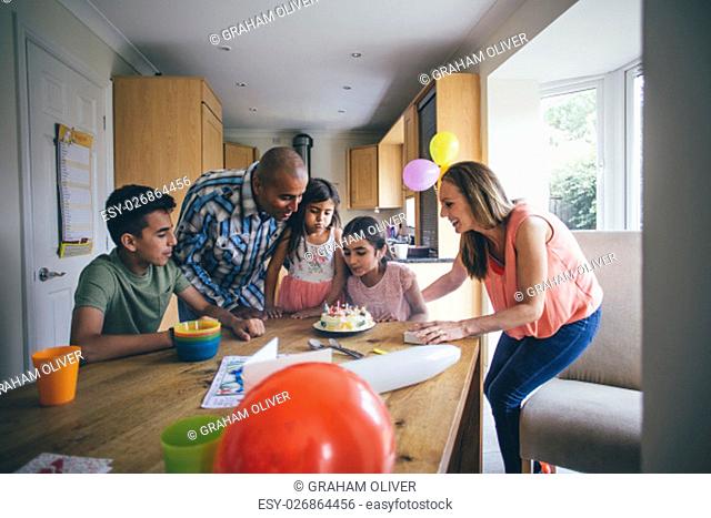 Family of five celebrating the sons birthday with a homemade cake. They are crowded round him as he blows out the candles
