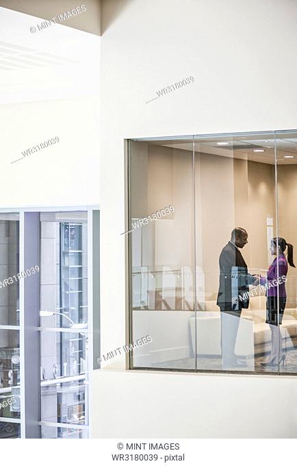 Black businessman and woman shaking hands in conference room window