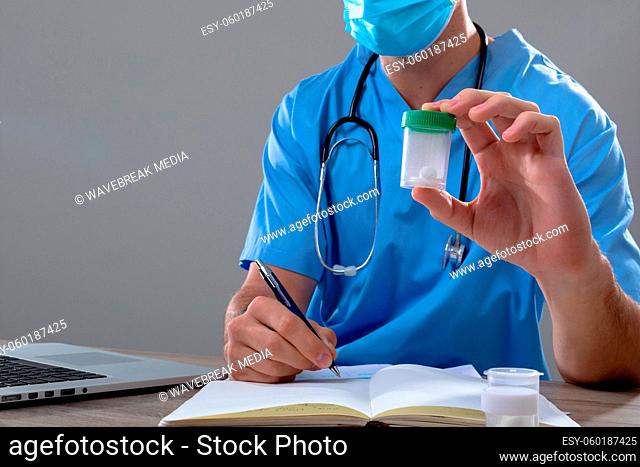 Caucasian male doctor wearing face mask holding box of pills