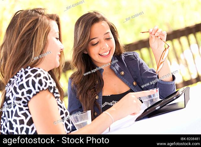 Expressive young adult girlfriends using their computer electronics outdoors