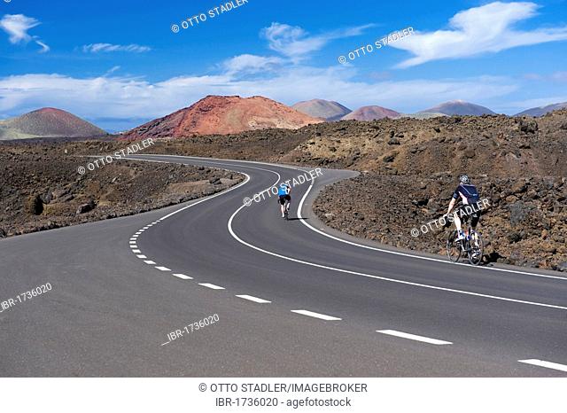 Cyclists on a road, volcanic landscape at Los Hervideros, Timanfaya National Park, Lanzarote, Canary Islands, Spain, Europe