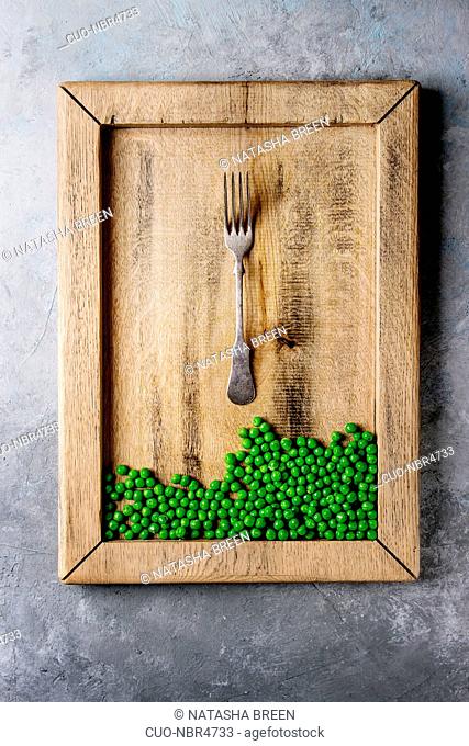 Raw uncooked organic green pea in wooden tray with fork over grey texture background. Top view, space. Diet concept