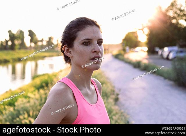 Confident sportswoman looking away while standing in park during sunset