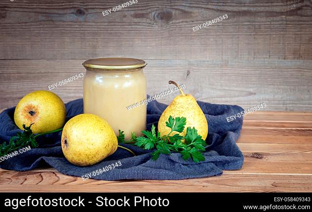Home preservation: glass jars with mashed ripe pears and three pears on a napkin on a wooden table