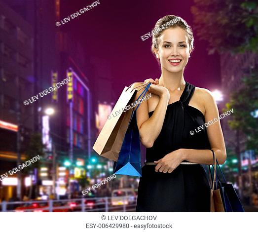 shopping, sale, gifts and holidays concept - smiling woman in evening dress with shopping bags over night city background
