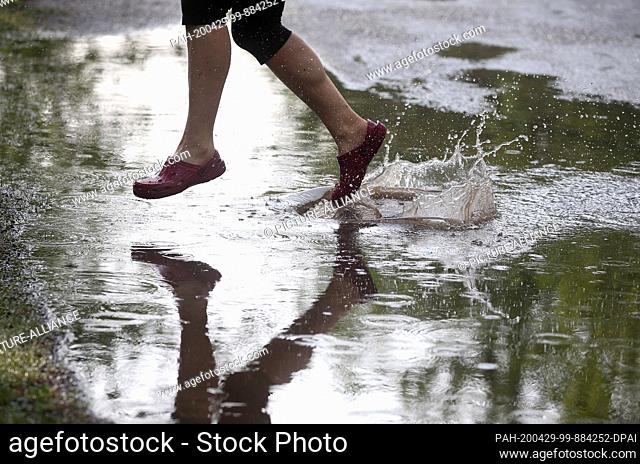 29 April 2020, Berlin: A young woman walks through large puddles of rain in the Köpenick district, which have formed on the streets after a heavy rain shower