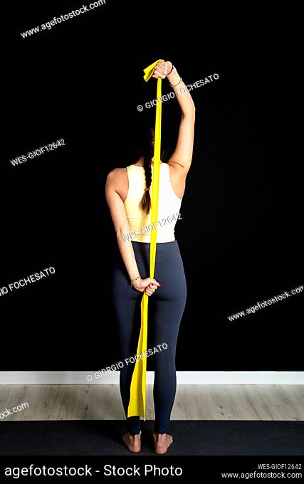 Young female athlete stretching yellow fabric while standing in studio