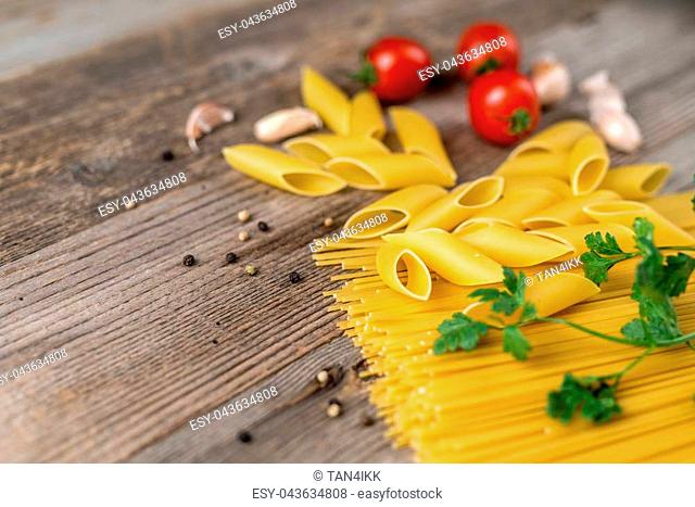 Various kinds of pasta and tomatoes and herbs uncooked on the wooden table, closeup
