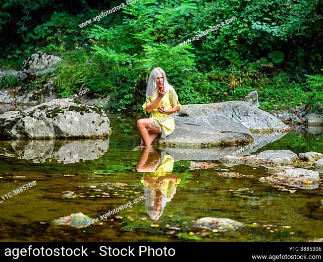 Attractive blonde woman on a Green forest river with an apple in hand