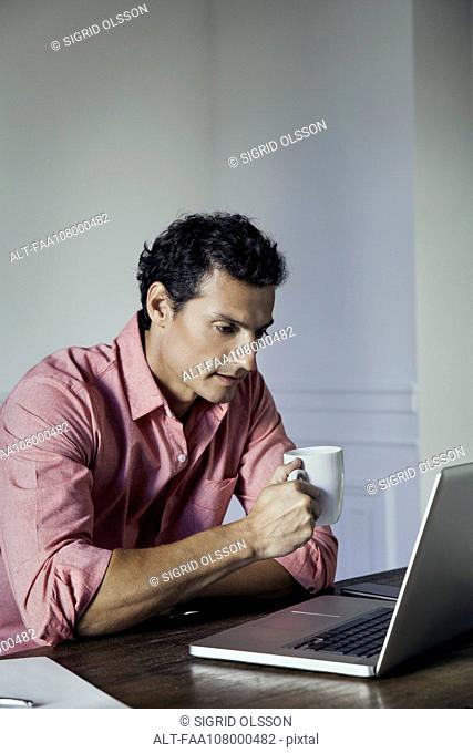 Man drinking coffee while using laptop computer