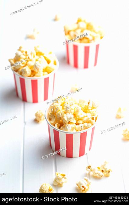 Sweet tasty popcorn in striped paper cup on white table