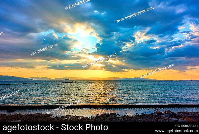 Beautiful sunset with the sun behind colorful clouds over the Aegan sea in Aegina island in Greece -- Panoramic sundown seascape - landscape