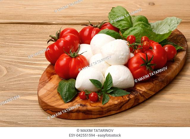Italian cuisine. Mozzarella, heirloom tomatoes, basil leaves on a wooden serving plate.Large depth of field