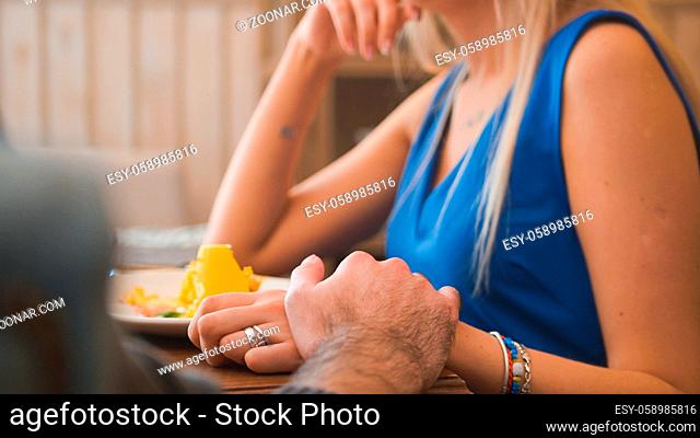 Holding hands of young couple in the cafe enjoying the desserts, close up