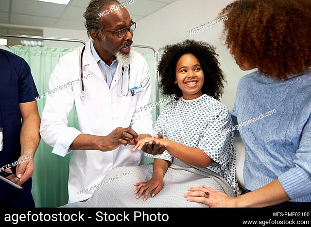 Doctor holding patient's hand talking to woman at hospital