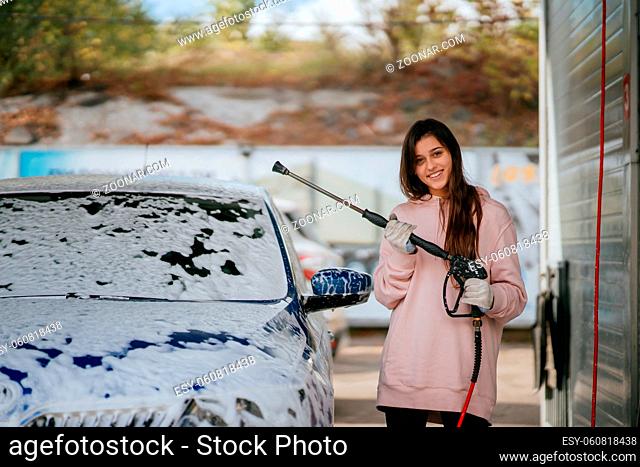 Brunette with long hair from a high-pressure hose applies a cleaner on the car at a car wash