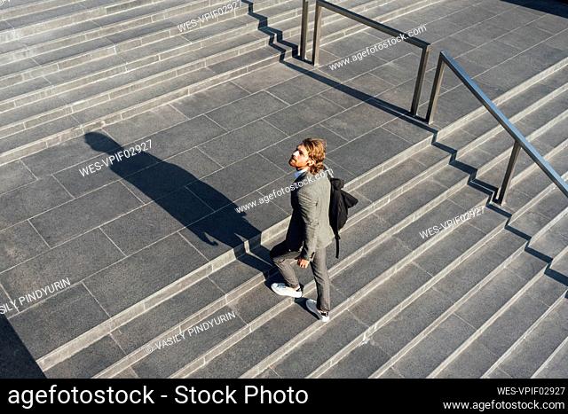Male entrepreneur with bag moving up on staircase while looking away in downtown during sunny day