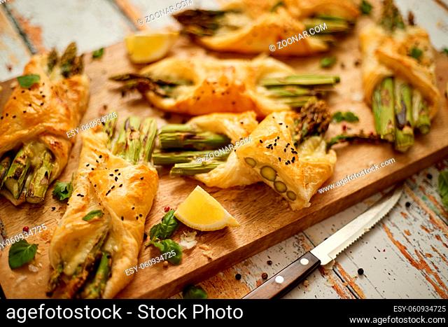 Baked green asparagus wrapped in puff pastry. Served on wooden board. Top view, flat lay. Selective focus