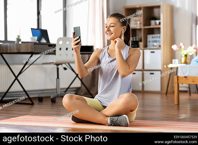 girl with phone and earphones exercising at home
