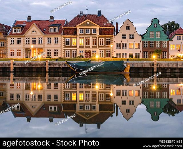 Germany, Schleswig-Holstein, Gluckstadt, Townhouses reflecting on shiny surface of river Elbe