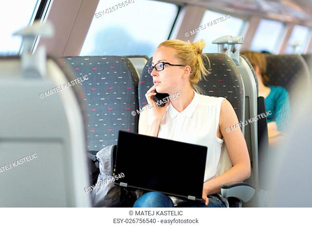 Businesswoman talking on cellphone and working on laptop while traveling by train. Business travel concept