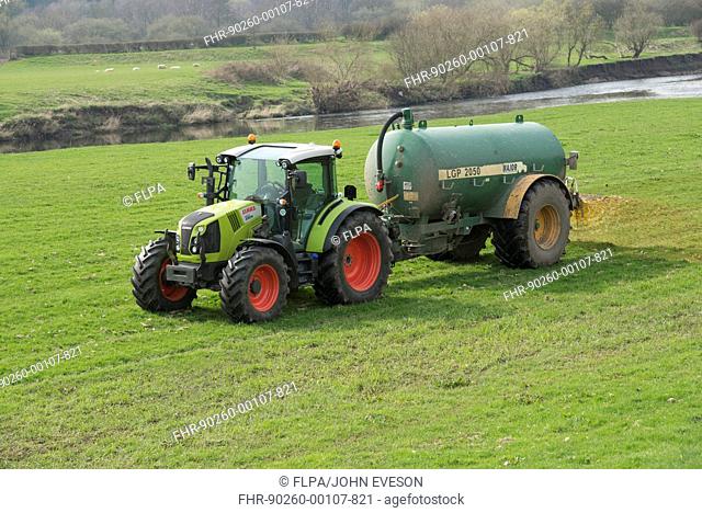Claas tractor with slurry tanker, spreading slurry on grassland near river, near Longridge, Lancashire, England, April