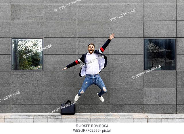 Excited businessman jumping in front of building