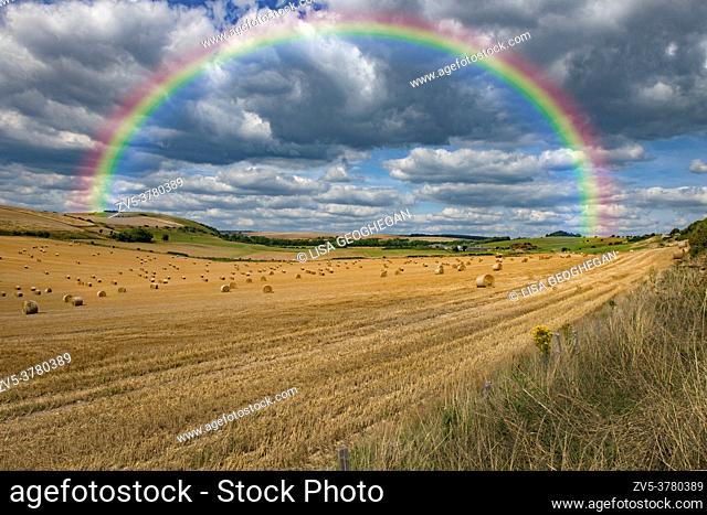 A landscape view of a field of hay bales underneath a rainbow on the South Downs at Clapham near Arundel, West Sussex. England. Uk