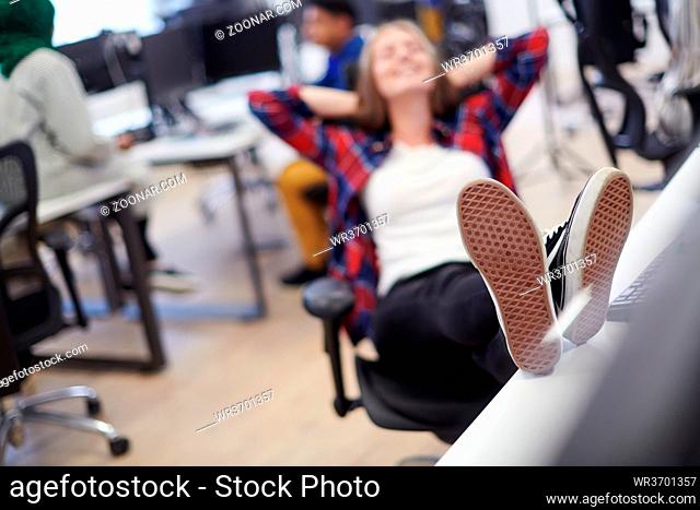 casual business woman taking a break with legs on her table while working on desktop computer in modern open plan startup office interior