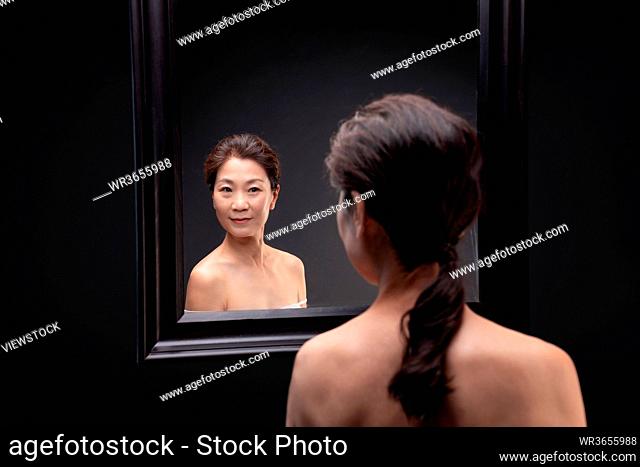 Elegant middle-aged woman look in the mirror
