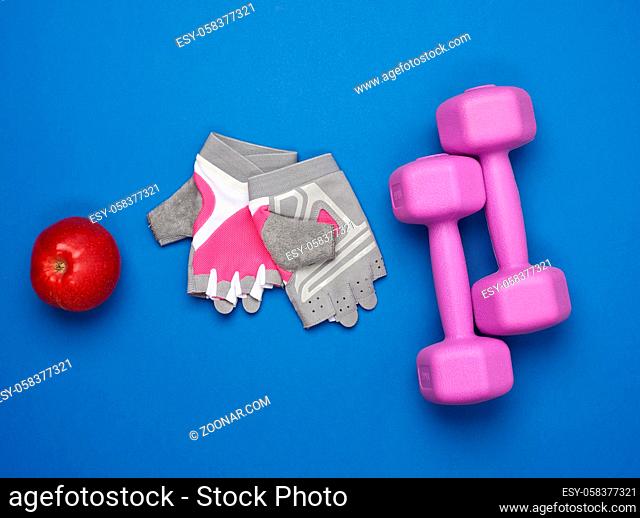 sports gloves, a pair of purple dumbbells and a red apple on a blue background, top view, healthy lifestyle