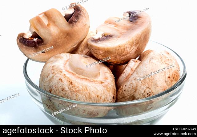 A few fresh raw mushrooms in a glass plate on a light background. Front view, close-up