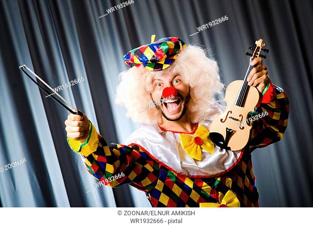 Funny clown plyaing violin against curtain