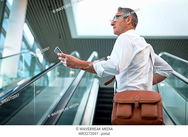 Businessman checking his mobile phone on the escalator
