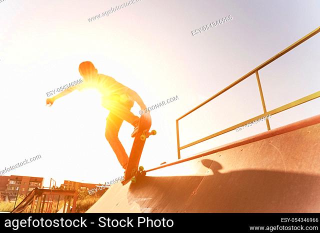 Teen skater hang up over a ramp on a skateboard in a skate park on sunset. Wide angle. Warm sunny picture