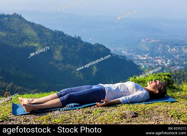 Woman relaxes in yoga asana Savasana, corpse pose outdoors in Himalayas. Himachal Pradesh, India, Asia