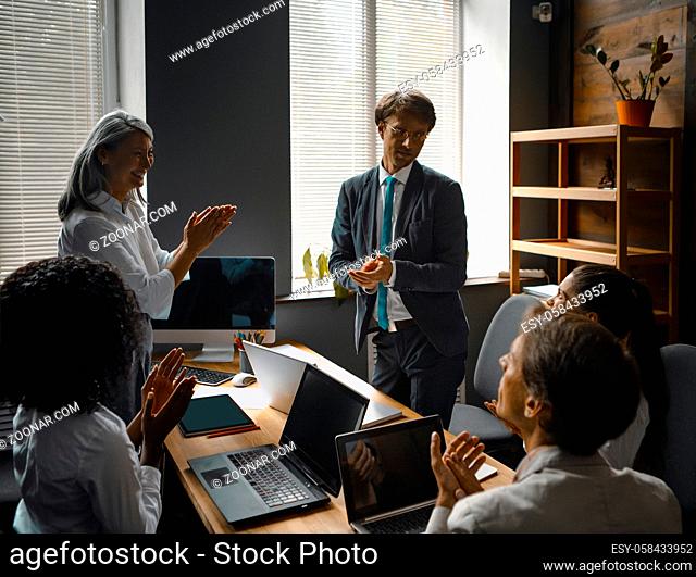 Group of business people congratulates applauds to a supervisor speech looking at computer with black screen at meeting. Supervisor of project happily receives...