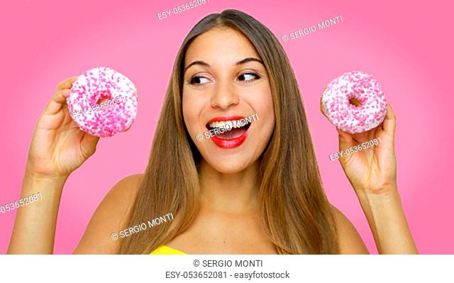 Happy cheerful excited young woman holding two donuts in her hands looking to the side on pink background