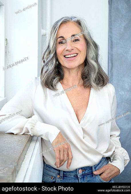 Smiling woman with gray hair standing by window
